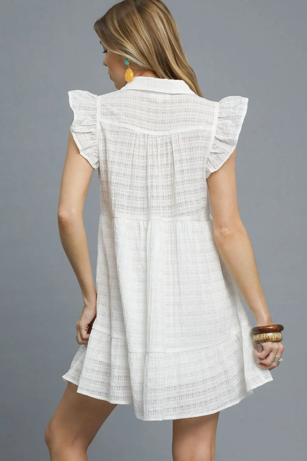 white mini dress features delicate ruffle cap sleeves and a classic button-front design that exudes feminine elegance. Crafted from lightweight textured fabric, it offers both comfort and style with its flattering empire waist silhouette