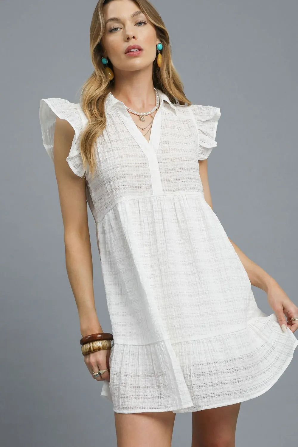 white mini dress features delicate ruffle cap sleeves and a classic button-front design that exudes feminine elegance. Crafted from lightweight textured fabric, it offers both comfort and style with its flattering empire waist silhouette